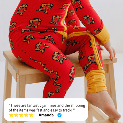 A child dressed in a Maryland Terrapins Onesie from Tailgate Tikes, featuring red pajamas with yellow cuffs and a bear print design, sits on a wooden stool. Amanda left a 5-star review stating, "These are fantastic jammies and the shipping of the items was fast and easy to track!" Perfect for your little Tailgate Tikes!