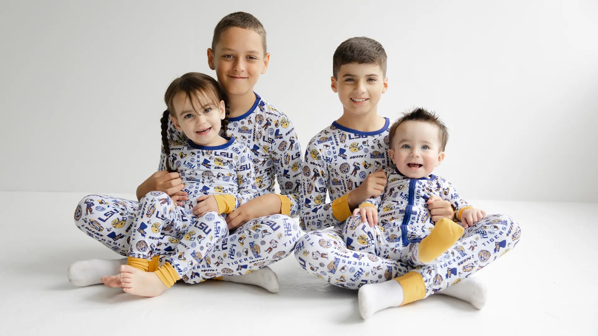 Four children wearing matching officially licensed LSU Tigers bamboo pajamas sitting on a white floor.