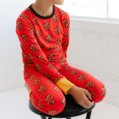 A child wearing a bright red long-sleeve pajama set with a repeating Maryland terrapins Testudo print, sitting on a black stool in a bright white room.