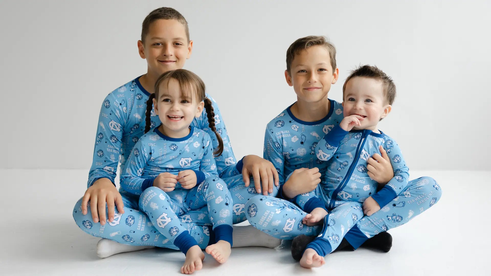 North Carolina Tar Heels bamboo baby and kids pajamas group photo featuring officially licensed zippy one-piece sleeper and two-piece pajama set in Carolina blue and white
