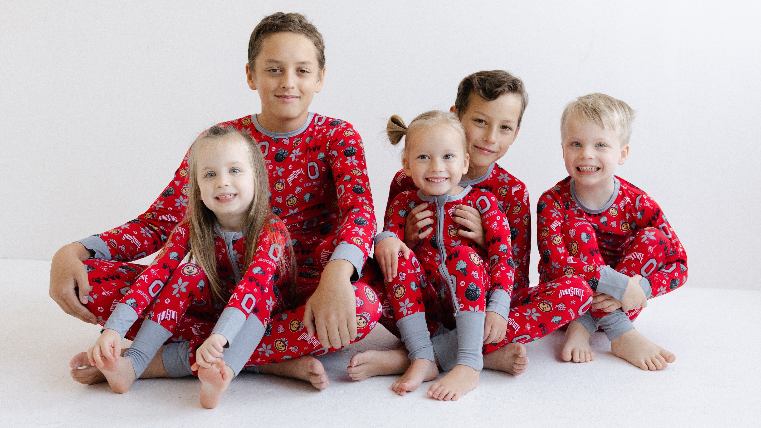 Five children sitting together wearing matching ohio state buckeyes bamboo long-sleeve pajamas with gray cuffs and legs, posed against a clean white studio background.