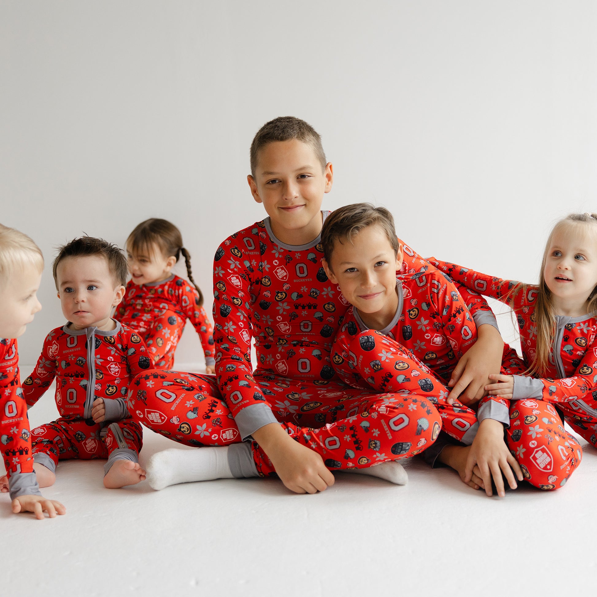 Children wearing ohio state buckeyes red pajamas with a pattern, sitting on a white floor.