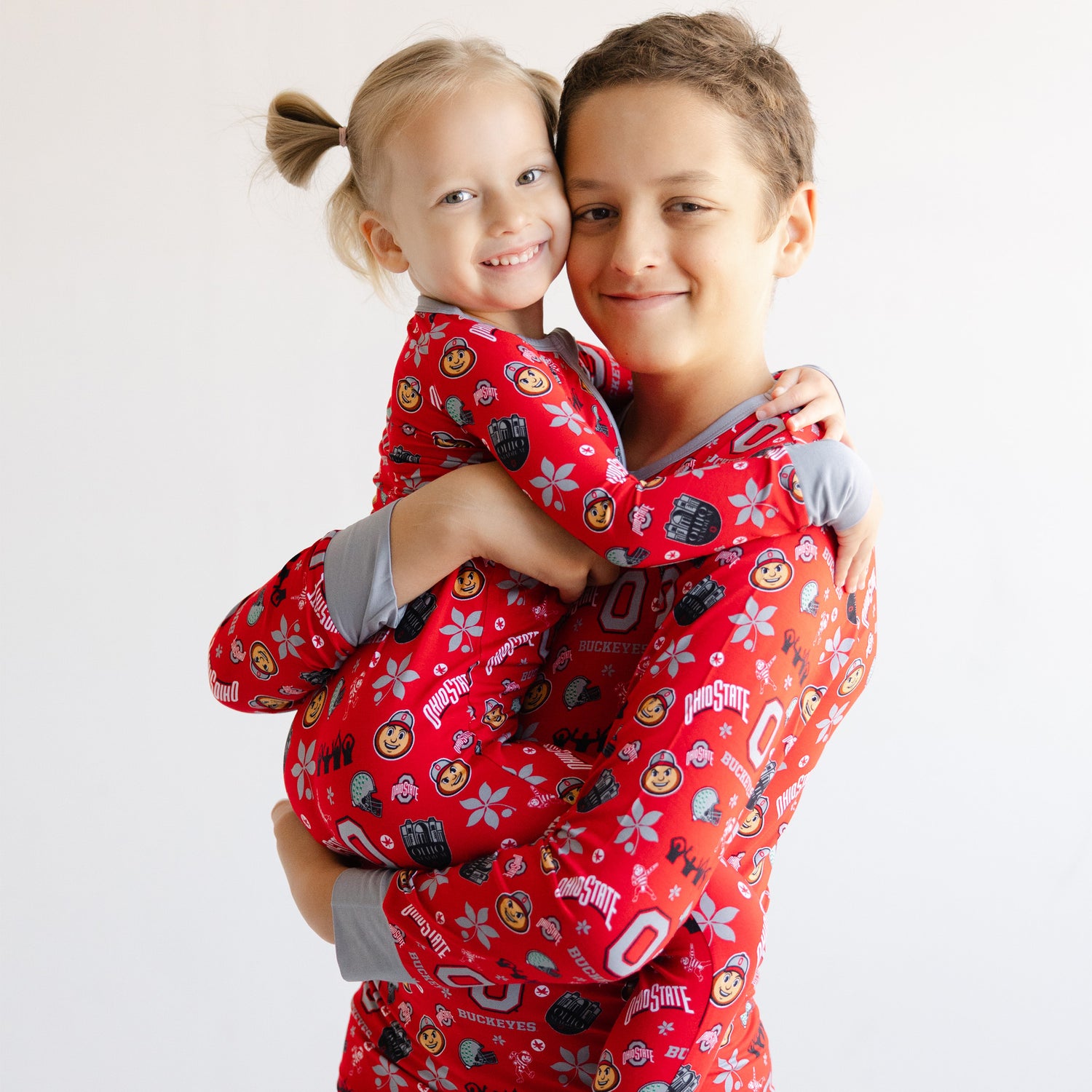 A young boy and girl wearing matching red Ohio State Buckeyes pajamas with a cartoon print, posed together against a plain white background.