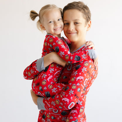 A young boy and girl wearing matching red Ohio State Buckeyes pajamas with a cartoon print, posed together against a plain white background.