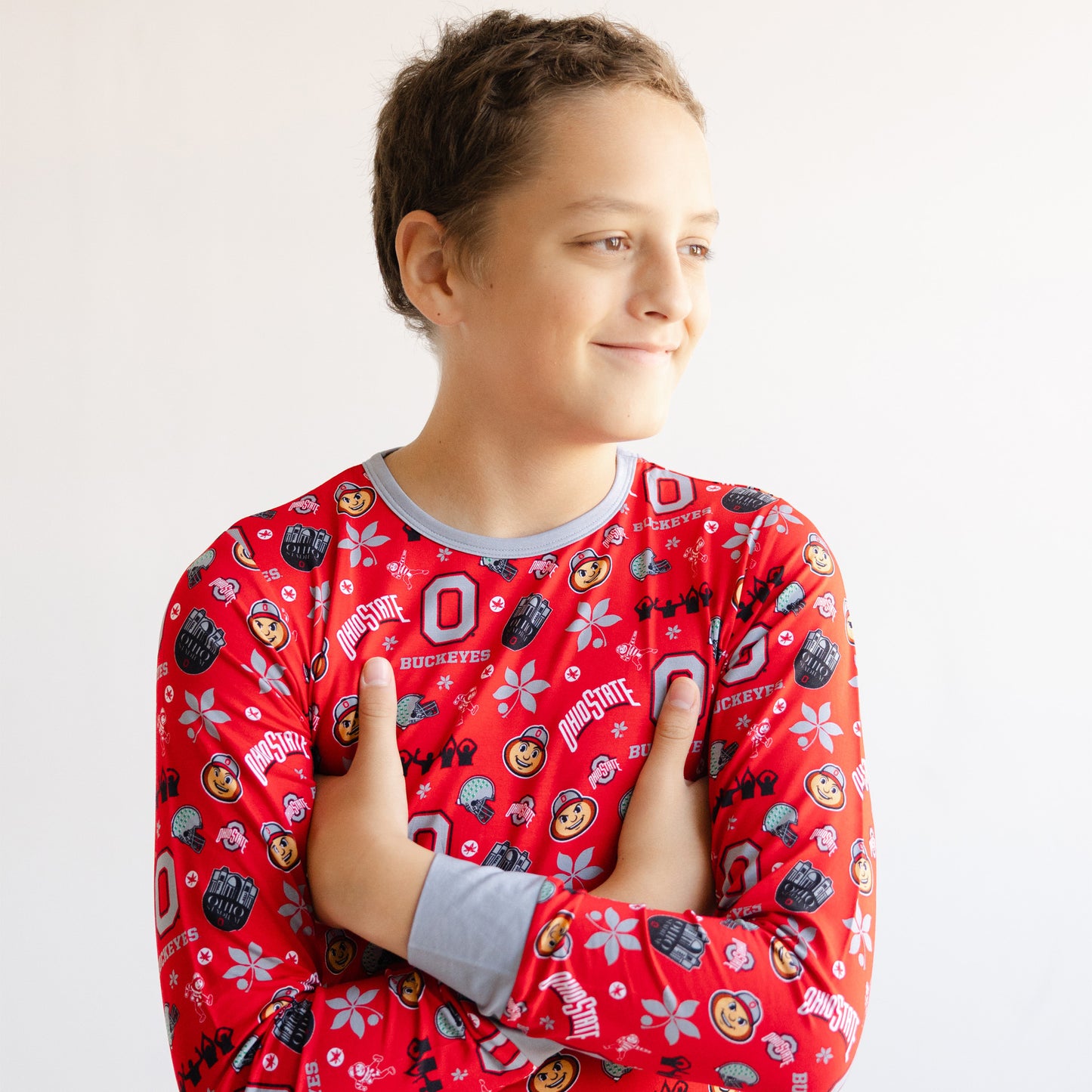 A child wearing a red long-sleeve pajama shirt with a colorful Ohio State Buckeyes football and hockey graphic print, posed against a plain white background.