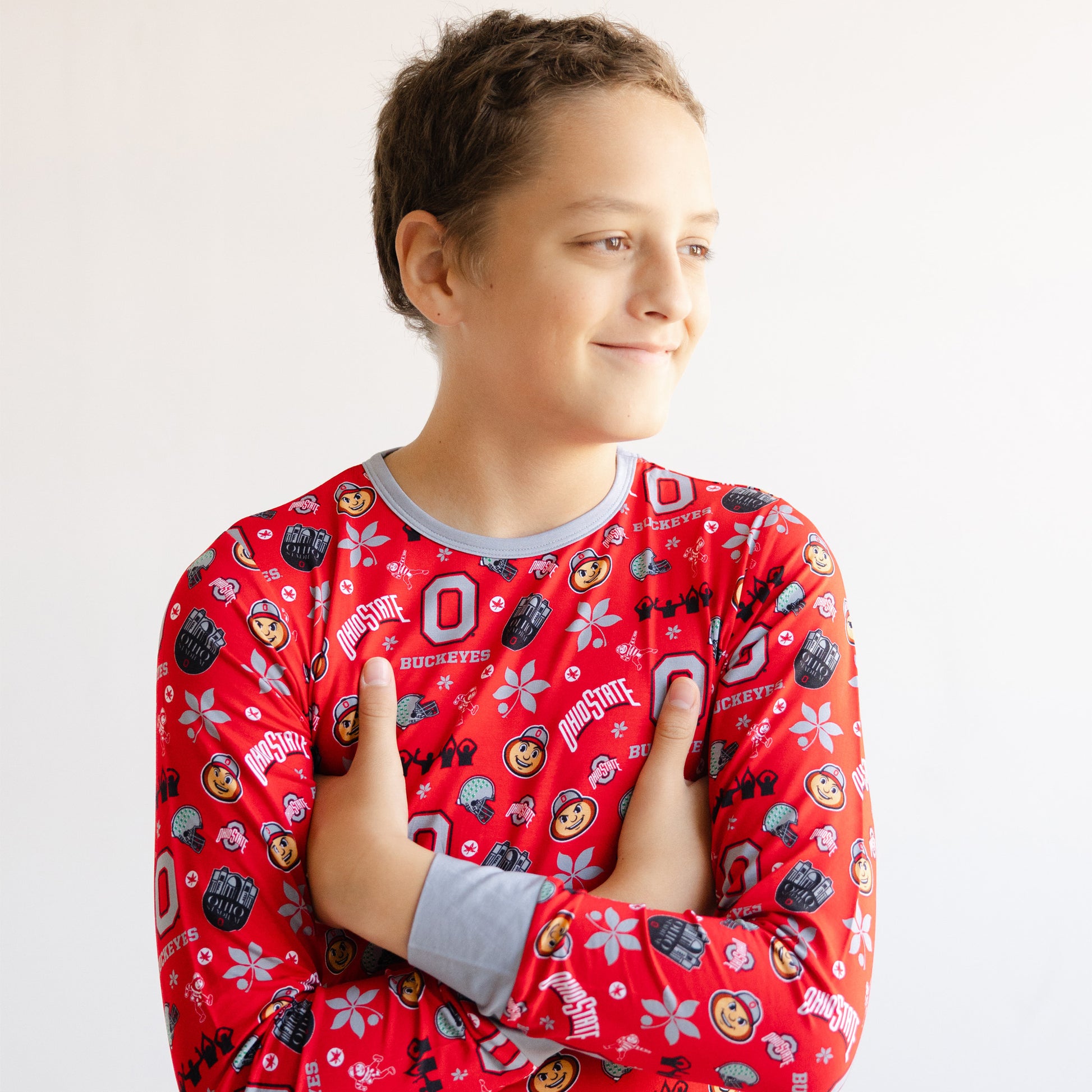 A child wearing a red long-sleeve pajama shirt with a colorful Ohio State Buckeyes football and hockey graphic print, posed against a plain white background.
