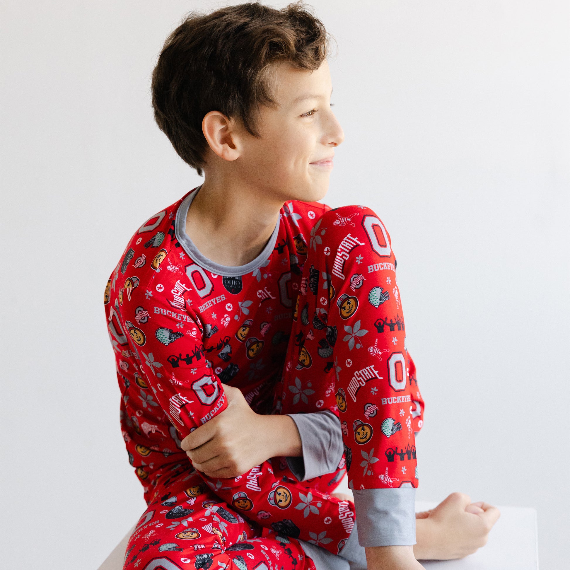 A young boy wearing a red long-sleeve officially licensed ohio state buckeyes bamboo pajamas sitting against a plain white background.