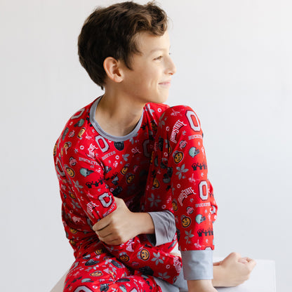 A young boy wearing a red long-sleeve officially licensed ohio state buckeyes bamboo pajamas sitting against a plain white background.