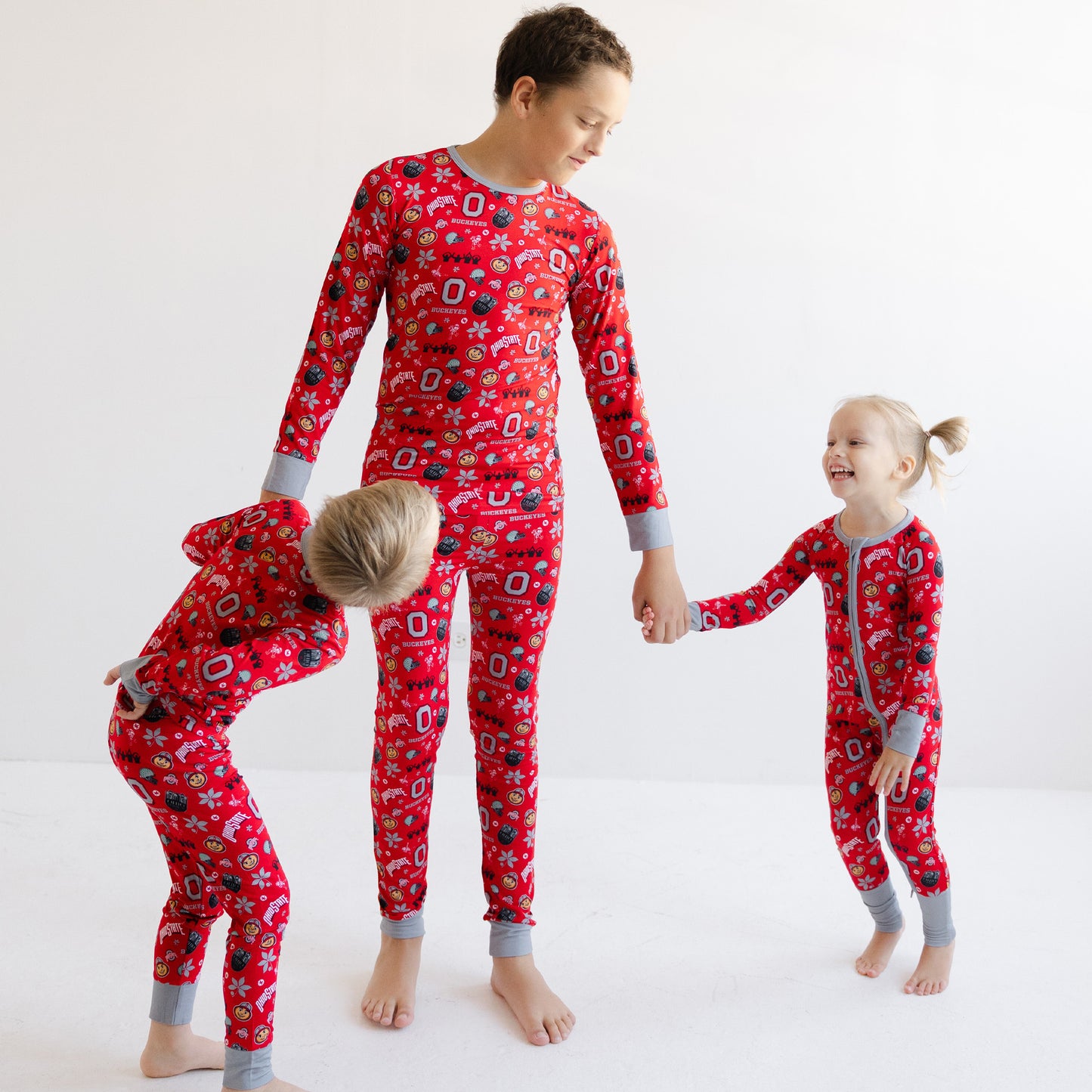 Three children wearing matching officially licensed ohio state buckeyes  and gray cuffs and collar, standing and bending on a white studio background.