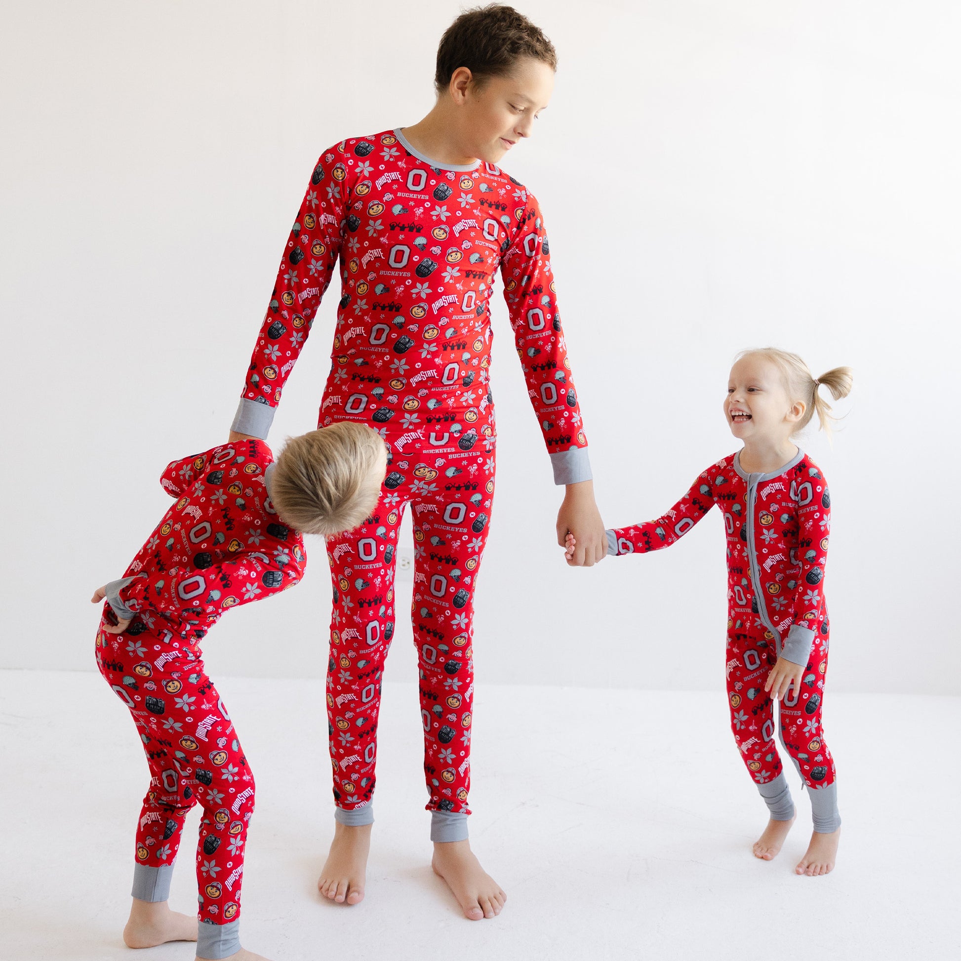 Three children wearing matching officially licensed ohio state buckeyes  and gray cuffs and collar, standing and bending on a white studio background.