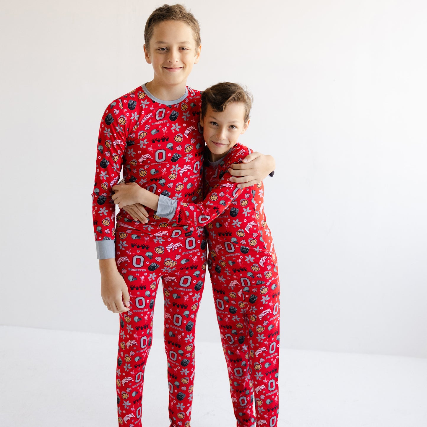 Two children standing together in matching officially licensed Ohio state buckeyes with a festive holiday print, photographed against a plain white studio background.