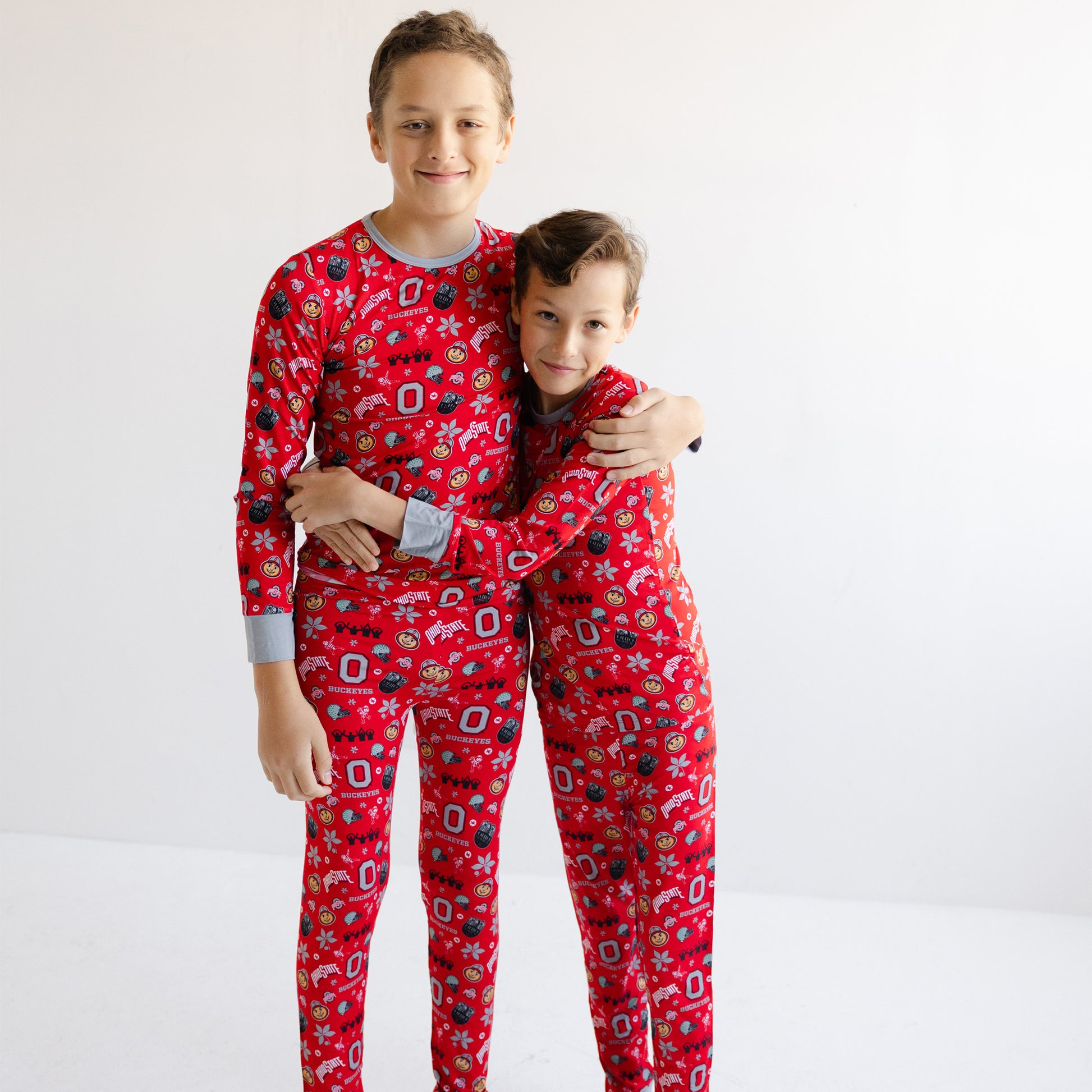 Two children standing together in matching officially licensed Ohio state buckeyes with a festive holiday print, photographed against a plain white studio background.