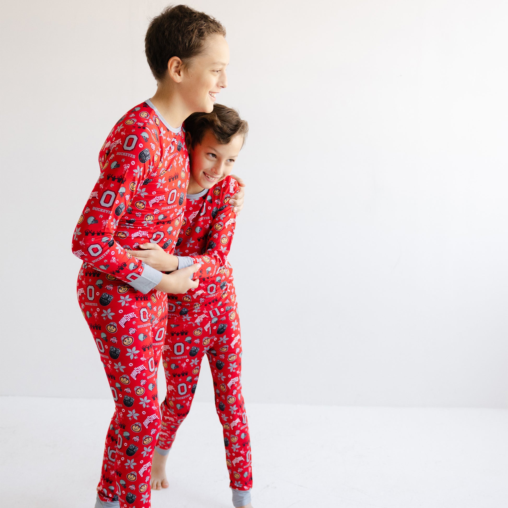 Two children wearing matching red long-sleeve pajamas with a ohio state buckeyes print, standing together against a plain white studio background.