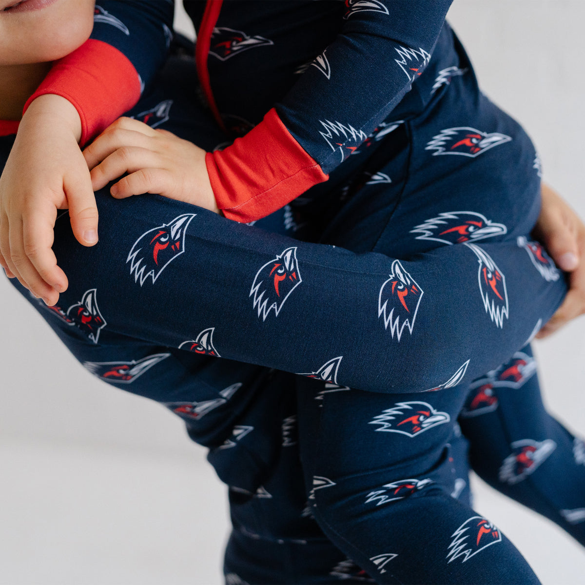 A close-up of a child wearing a navy UTSA roadrunners bamboo zipper one piece sleeper.