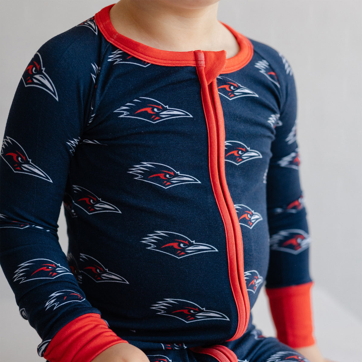 A close-up of a child wearing a navy UTSA roadrunners bamboo zipper one piece sleeper.
