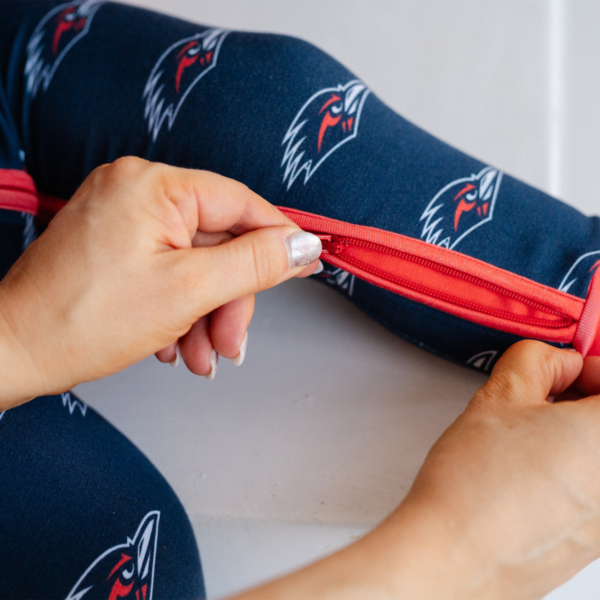 Close-up of a person unzipping UTSA roadrunners bamboo zipper one piece sleeper.
