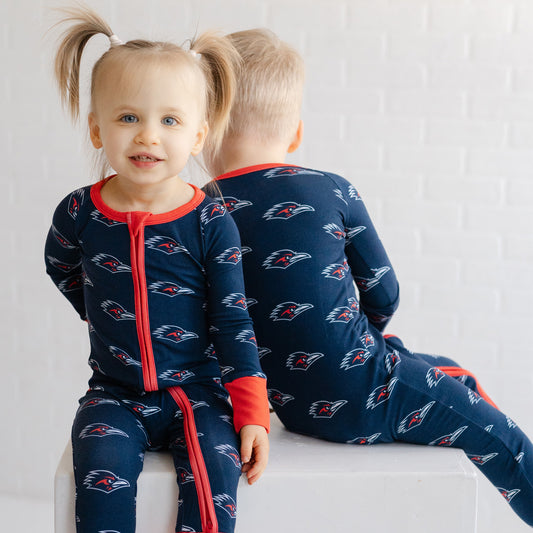 Two children wearing matching navy UTSA roadrunners bamboo zipper one piece sleeper.