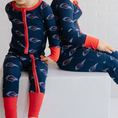 Two children wearing matching navy UTSA roadrunners bamboo zipper one piece sleepers.